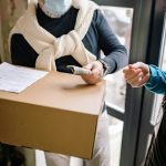 Senior man with facemask receiving a package and making payment indoors.